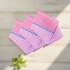 Three red check 22x22 cotton handkerchiefs neatly folded on a soft, neutral lifestyle background.